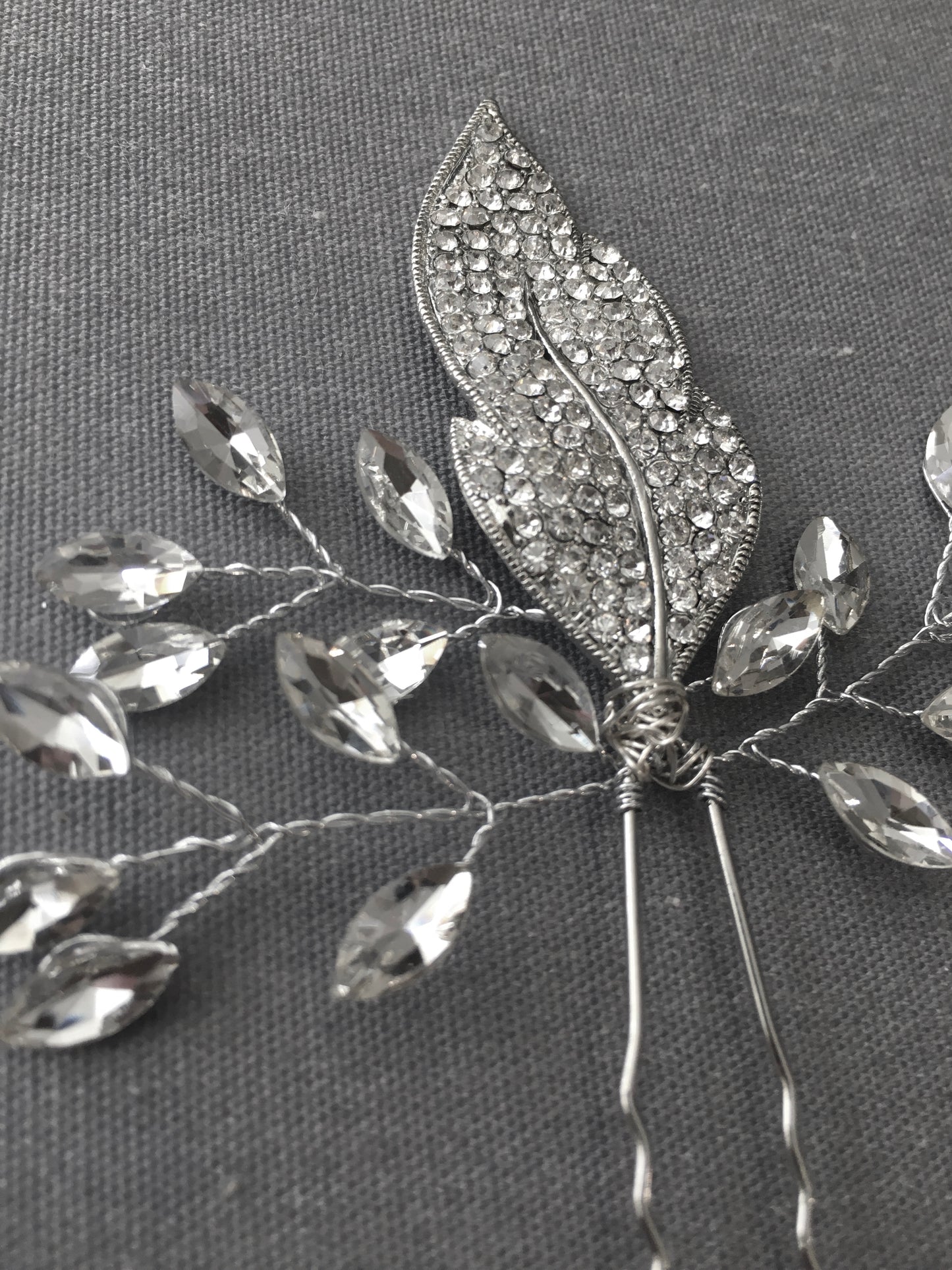 Decorative hairpin with leaf design and crystal-like stones on a gray background